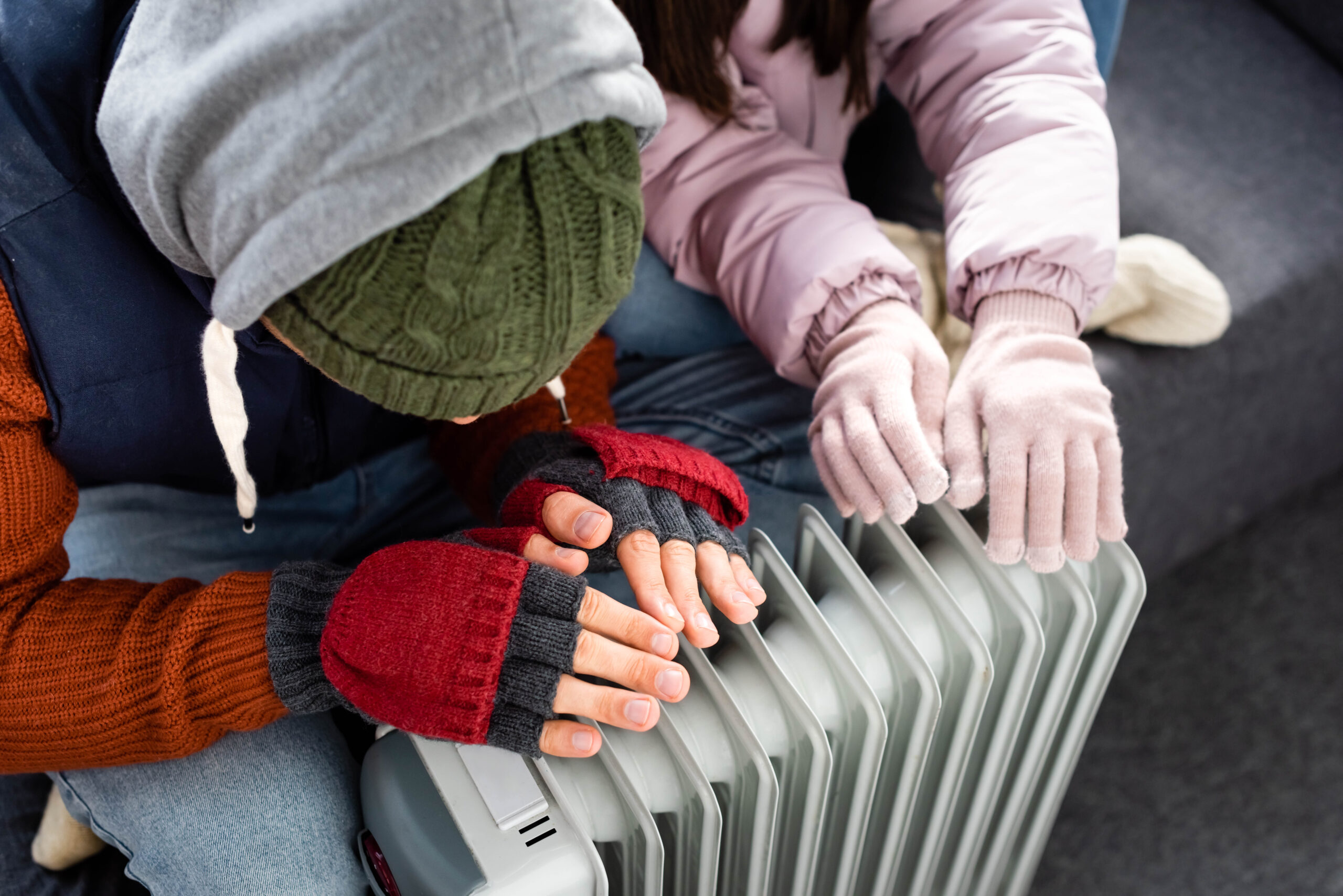 high angle view of girlfriend and boyfriend in winter outfit warming up near heater
